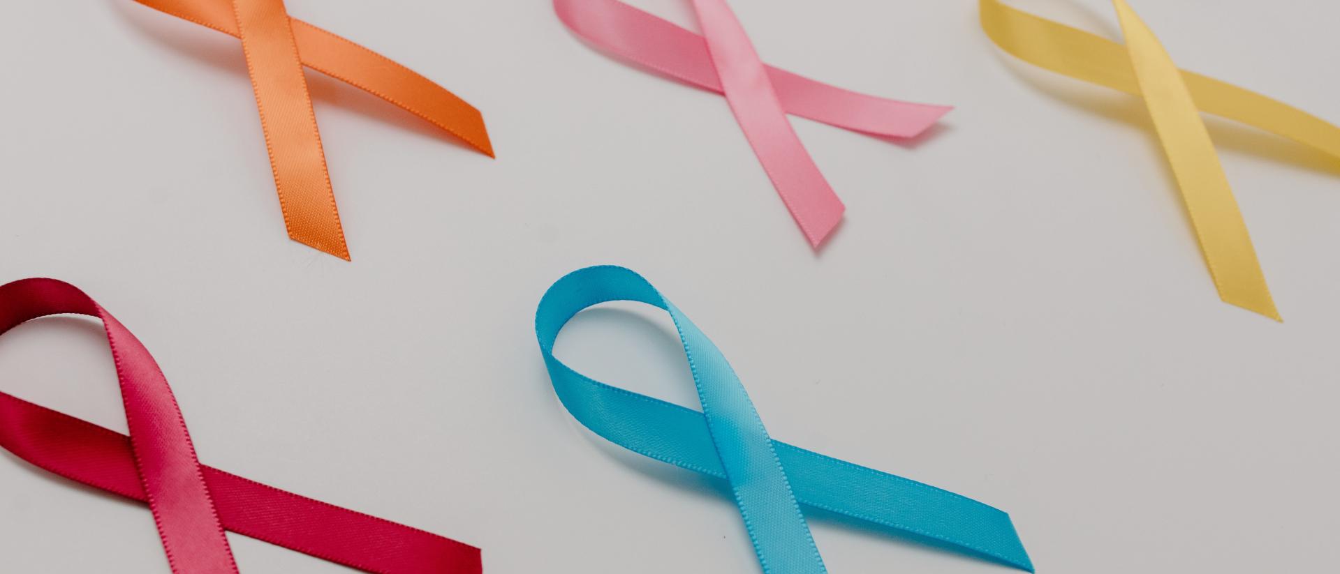 Viele bunte Schleifen liegen auf einem Tisch. Jedes einzelne Krebs Ribbon steht mit seiner Farbe für unterschiedliche Krebsarten.