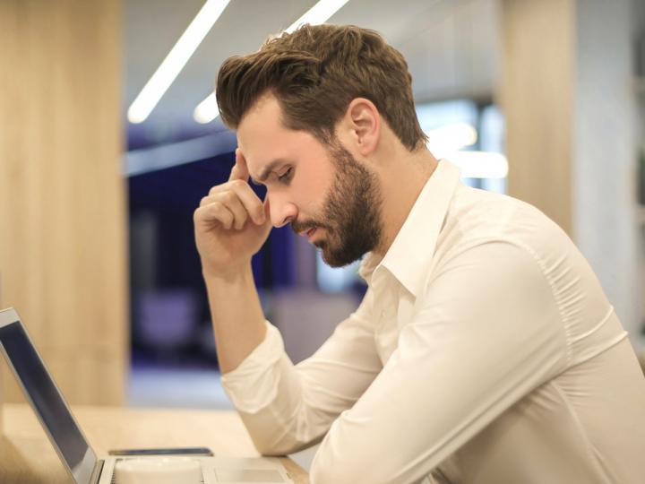 Junger Mann brütet nachdenklich vor Laptop