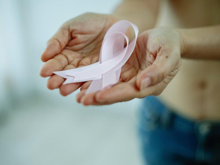 Zwei geöffnete Hände halten eine rosa Krebsschleife