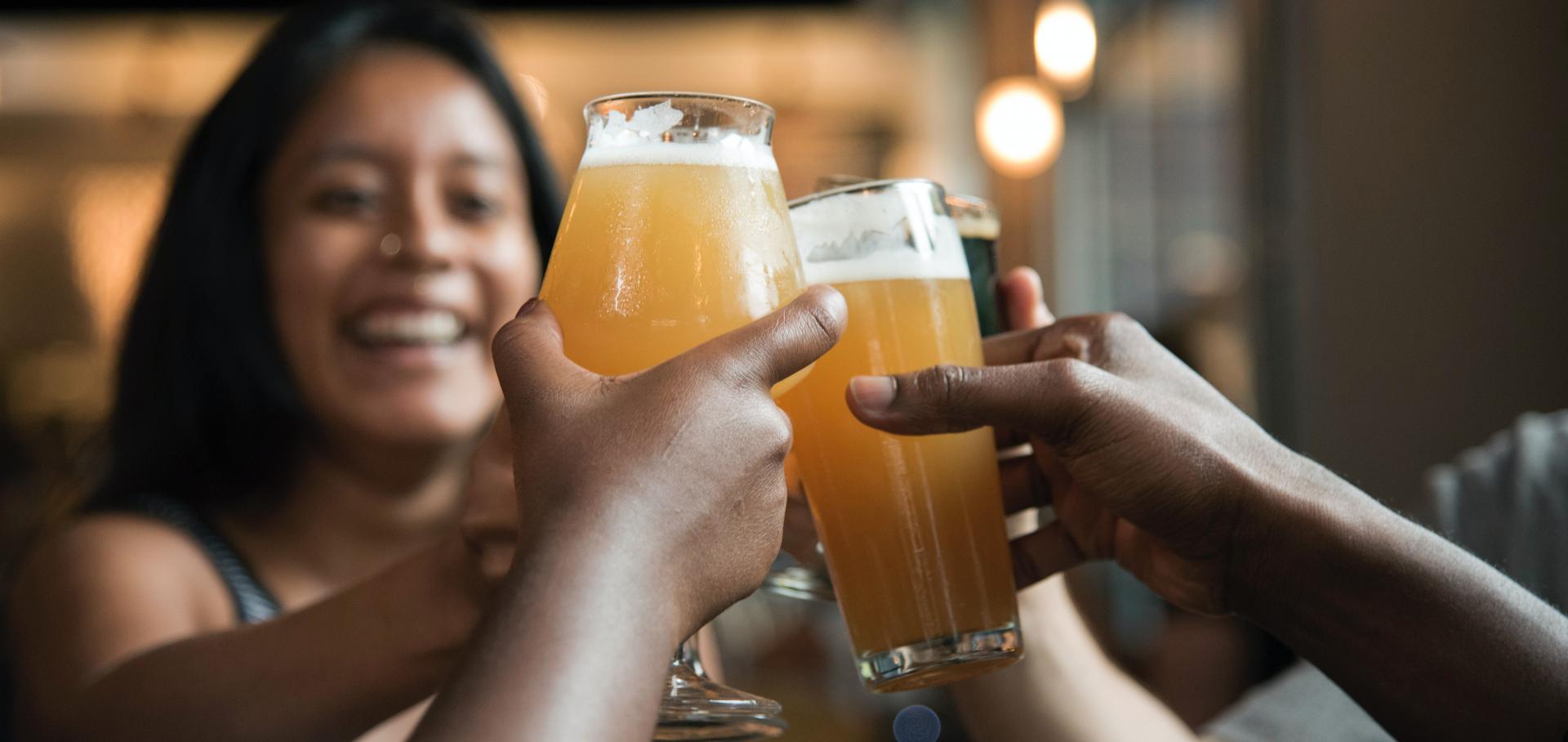 Eine junge Frau stößt mit ihren Freunden glücklich mit einem Bier an.