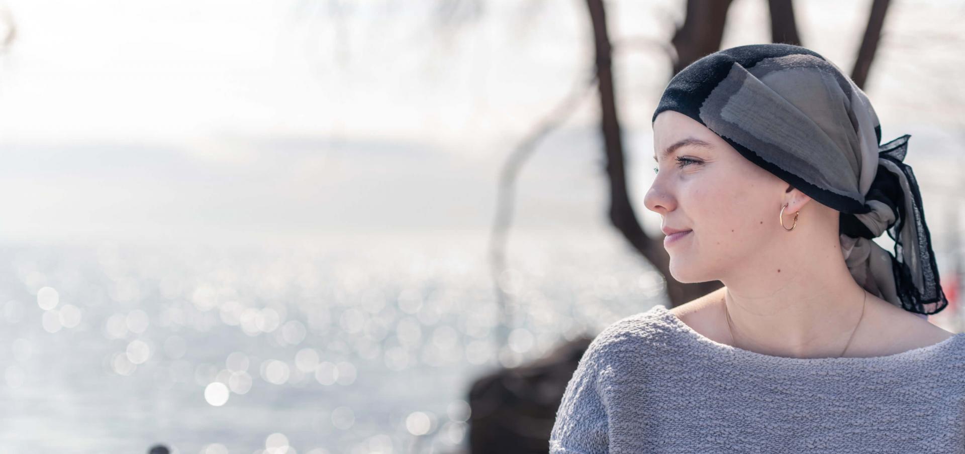 Eine Frau mit Krebserkrankung trägt ein Kopftuch und blickt zuversichtlich auf das Meer hinaus