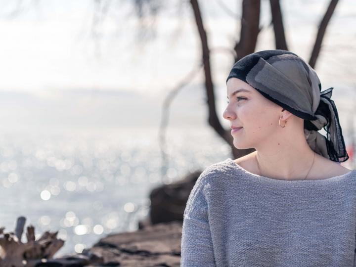 Eine Frau mit Krebserkrankung trägt ein Kopftuch und blickt zuversichtlich auf das Meer hinaus