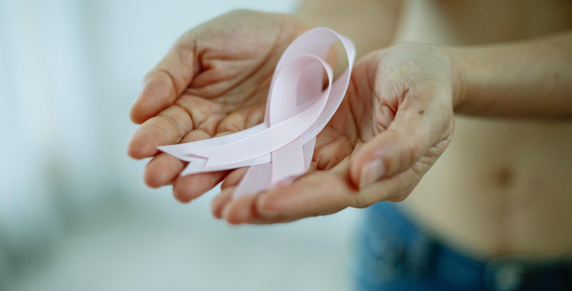 Hände formen behutsam eine Schale um die rosa Krebs Ribbons zu halten. Rosa Krebsschleifen stehen für Brustkrebs.