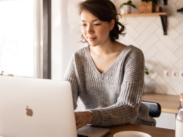 Eine junge Frau sitzt in der Küche an ihrem Laptop und informiert sich über die Krebsversicherung