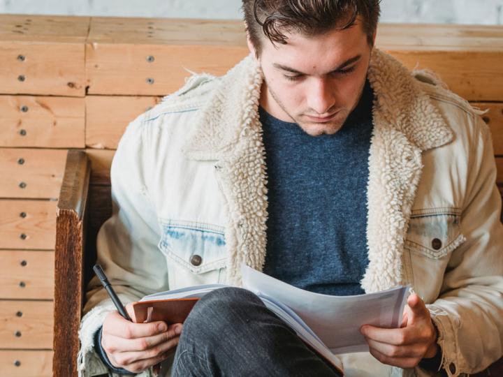Ein junger Mann sitzt auf einer Bank und konzentriert sich auf Unterlagen, die er in seinen Händen hält. Er informiert sich über verschiedene Versicherungen.