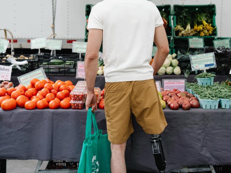Junger Mann mit Unterschenkelprothese steht vor Gemüseauslage