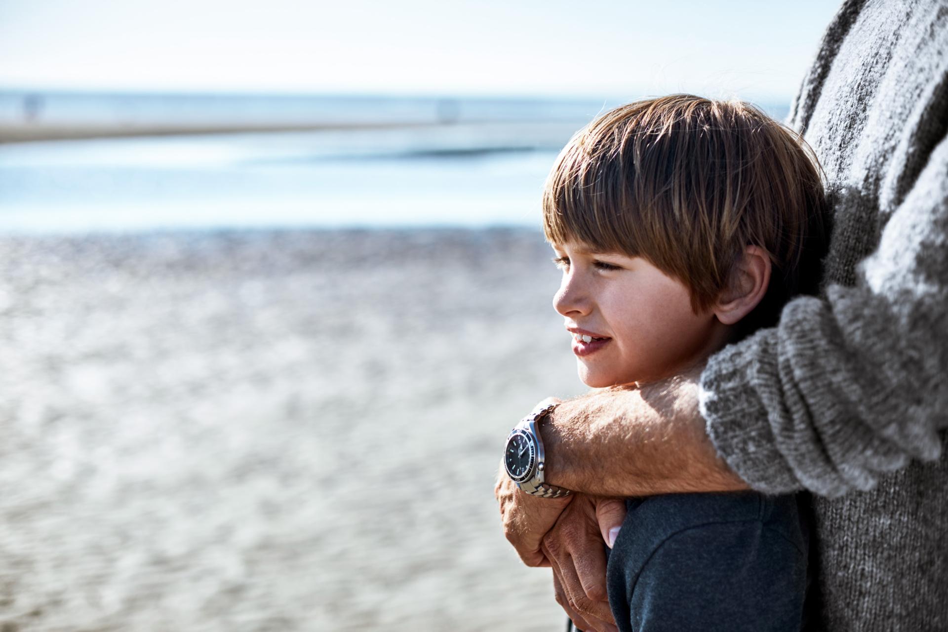 Junge steht mit seinem Vater am Meer und schaut in die Ferne