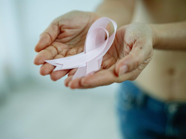 Zwei geöffnete Hände halten eine rosa Krebsschleife