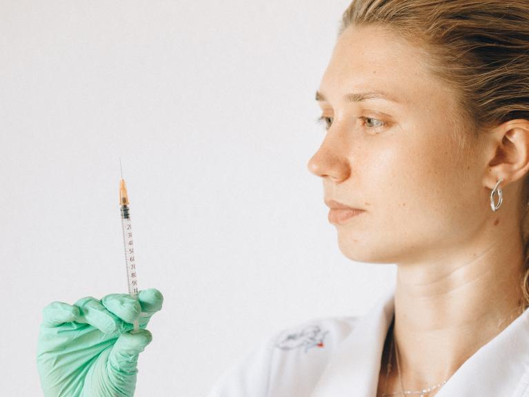 Eine junge Frau trägt Laborkleidung und hält eine Spritze in der Hand
