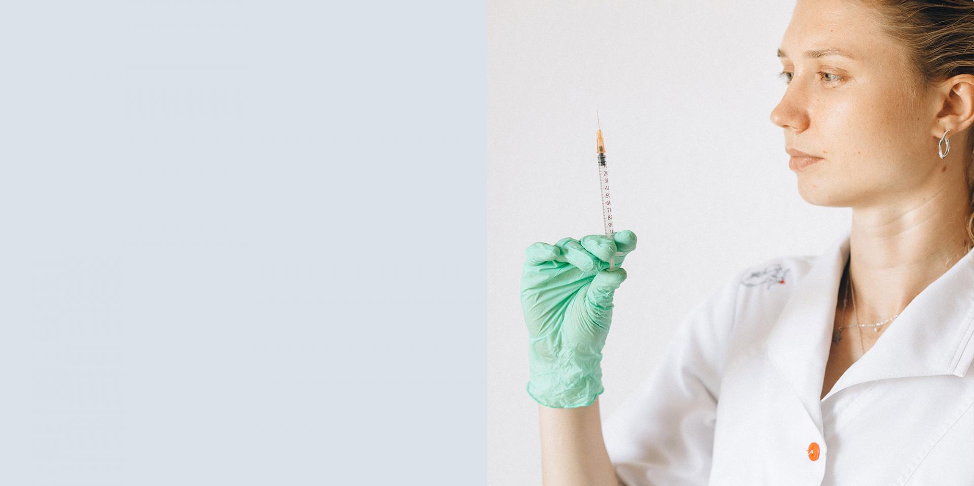 Eine junge Frau trägt Laborkleidung und hält eine Spritze in der Hand