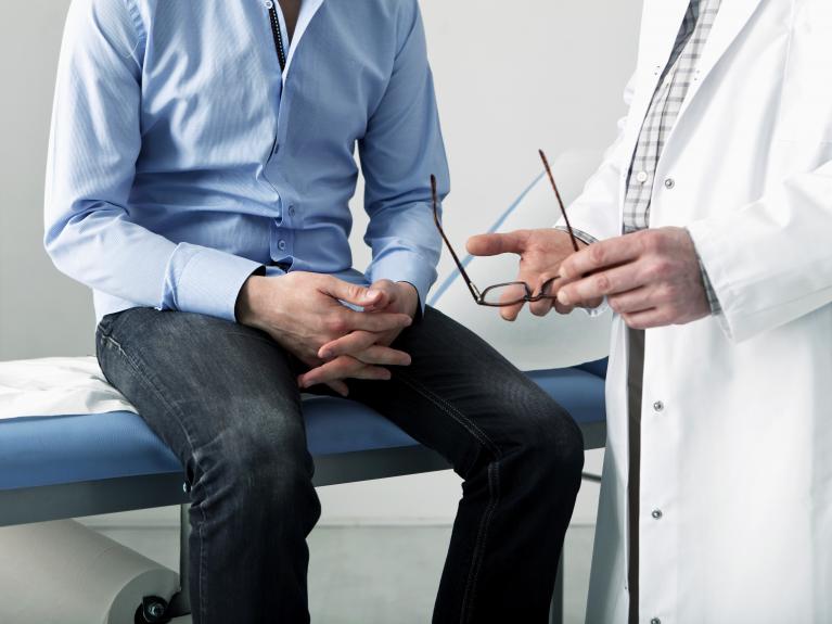 Ein Mann sitzt auf der Untersuchungsliege und wird von seinem Arzt beraten.